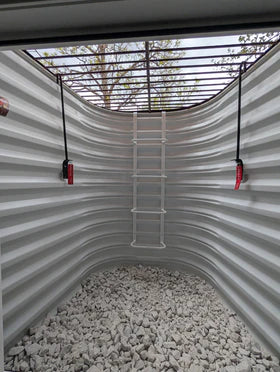 Interior view of a basement egress window well with grate locks and a ladder, showcasing egress window well grate locks with emergency release.